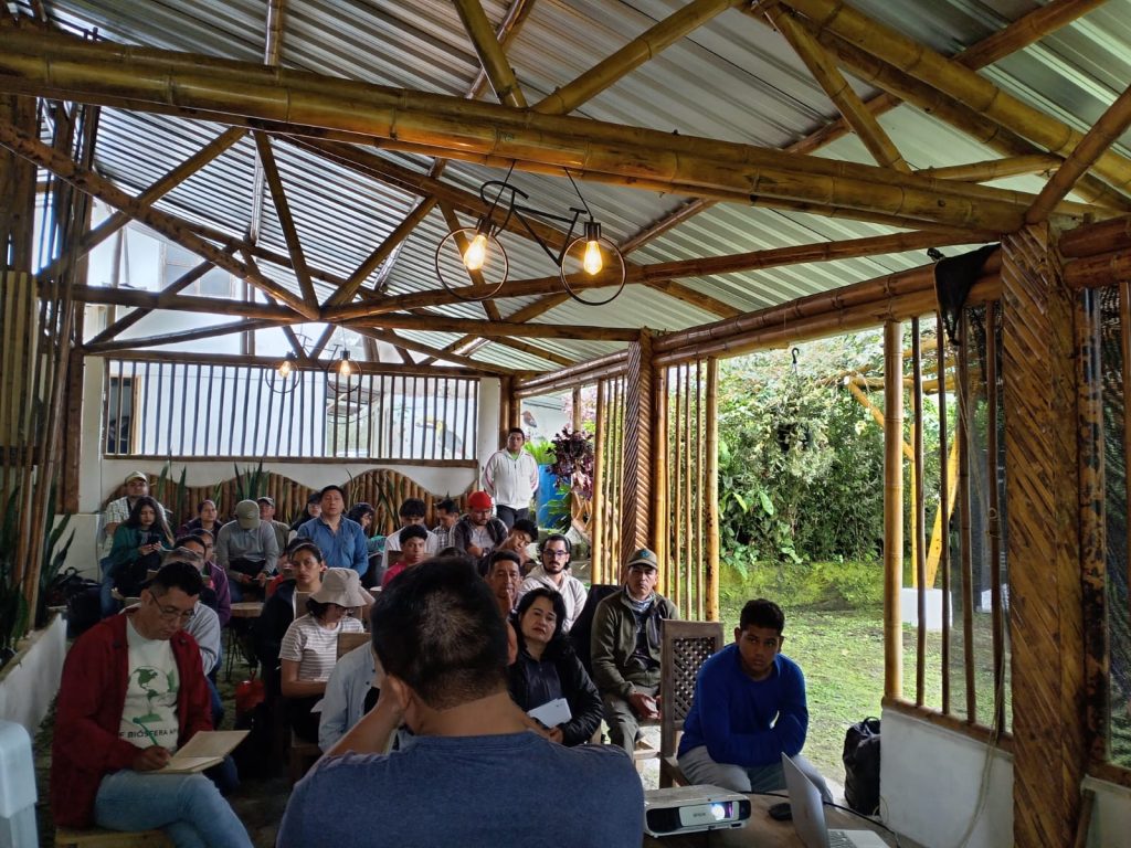 Die Teilnehmenden des Workshops sitzen in einem halb offenen Raum, gebaut aus Bambus, und hören den Vortragenden zu.